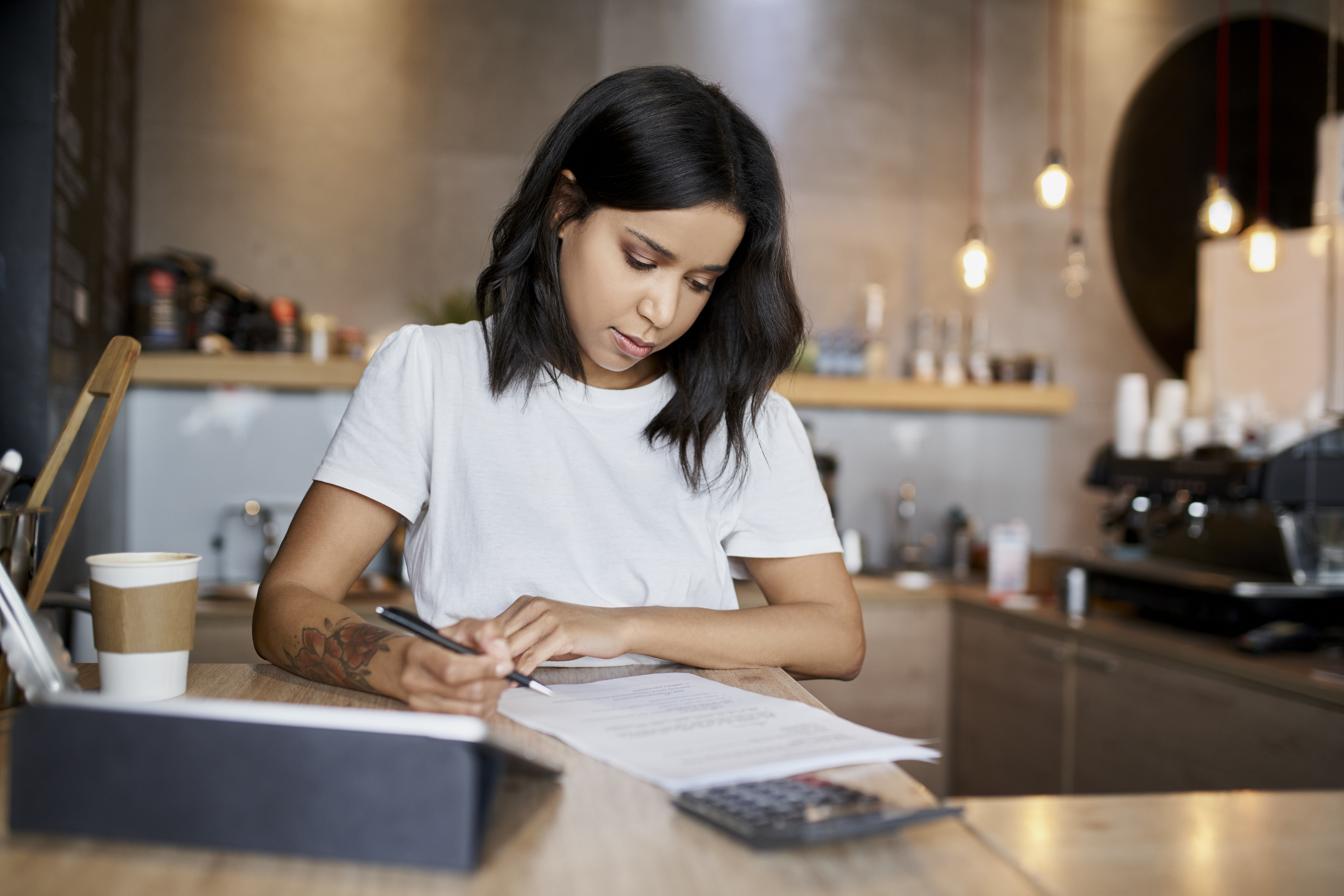Female cafe owner signing papers calculating business expenses Female cafe owner signing papers calculating business expenses